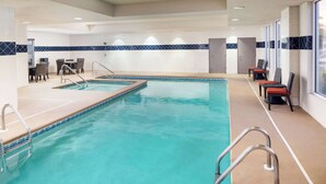 Una piscina con agua azul cristalina, rodeada de sillas de descanso y un área de comedor con mesas y sillas.