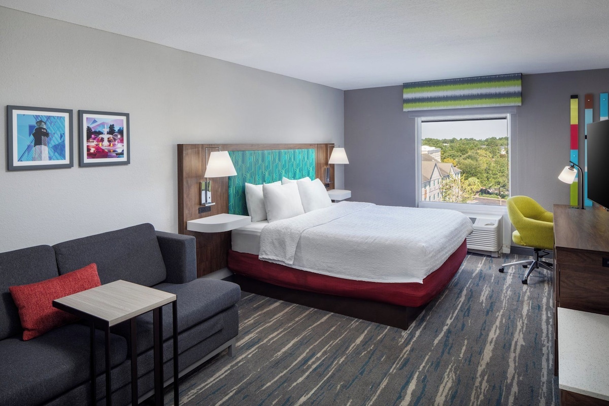 A hotel room with a bed, a desk, a chair, a sofa, and a window with a view.