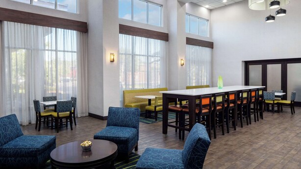 Un espacioso vestíbulo de hotel con techos altos, grandes ventanales y diversas opciones de asientos, incluyendo sofás y sillones.