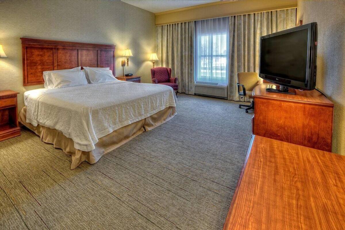 A hotel room with a large bed, a television on a wooden stand, a desk, and a chair.