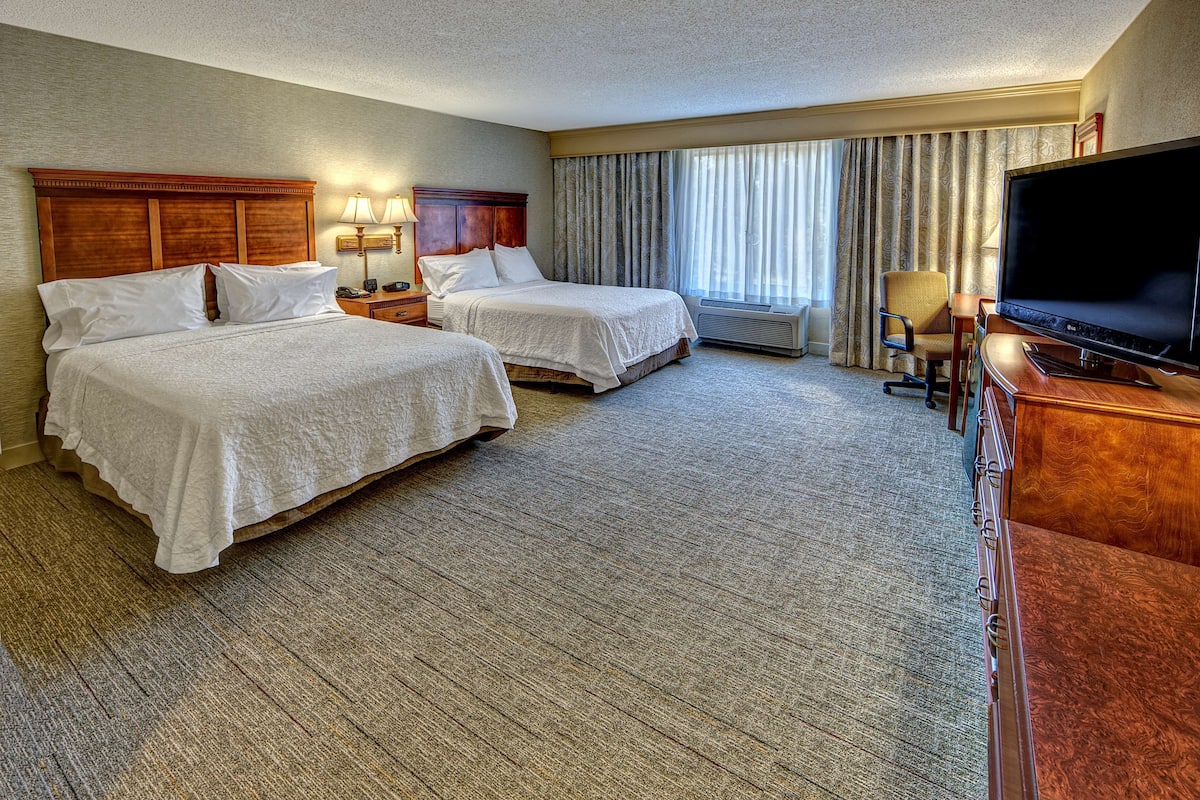 A hotel room with two beds, a TV, a desk, and a chair.