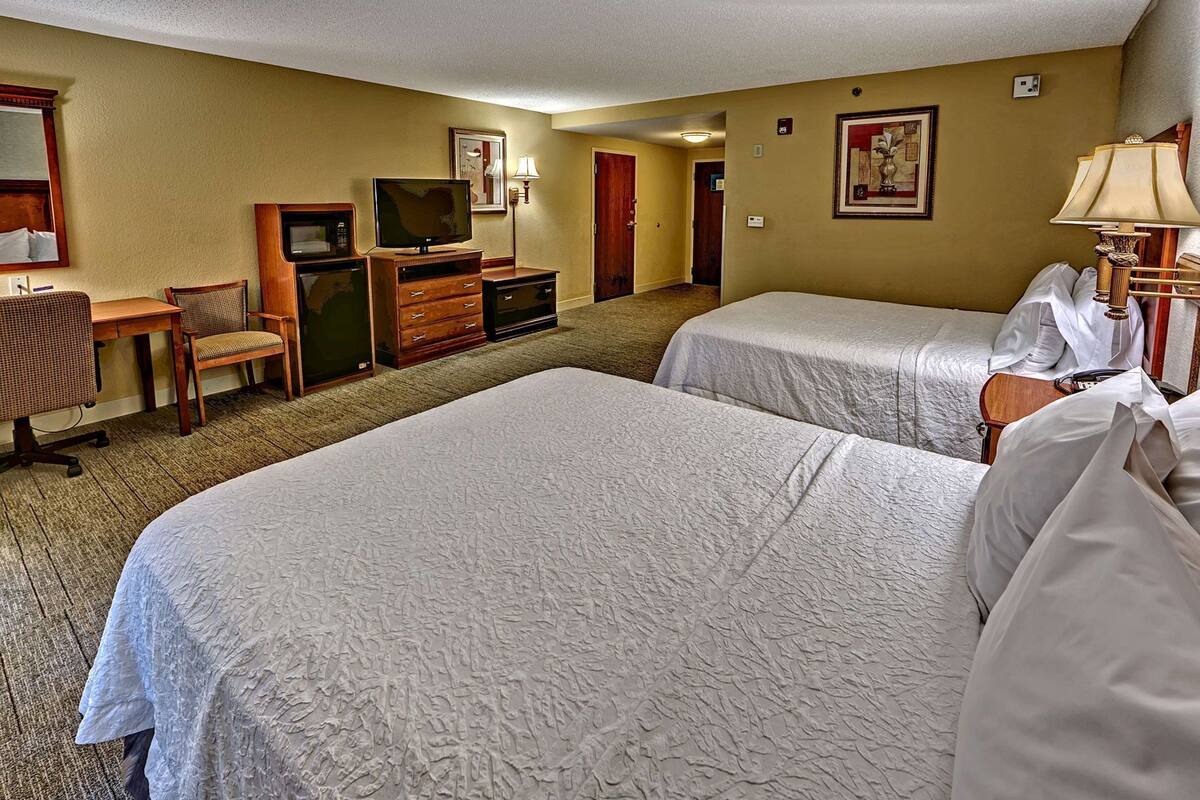 A hotel room with two beds, a desk with a television, a chair, a dresser, and a lamp.