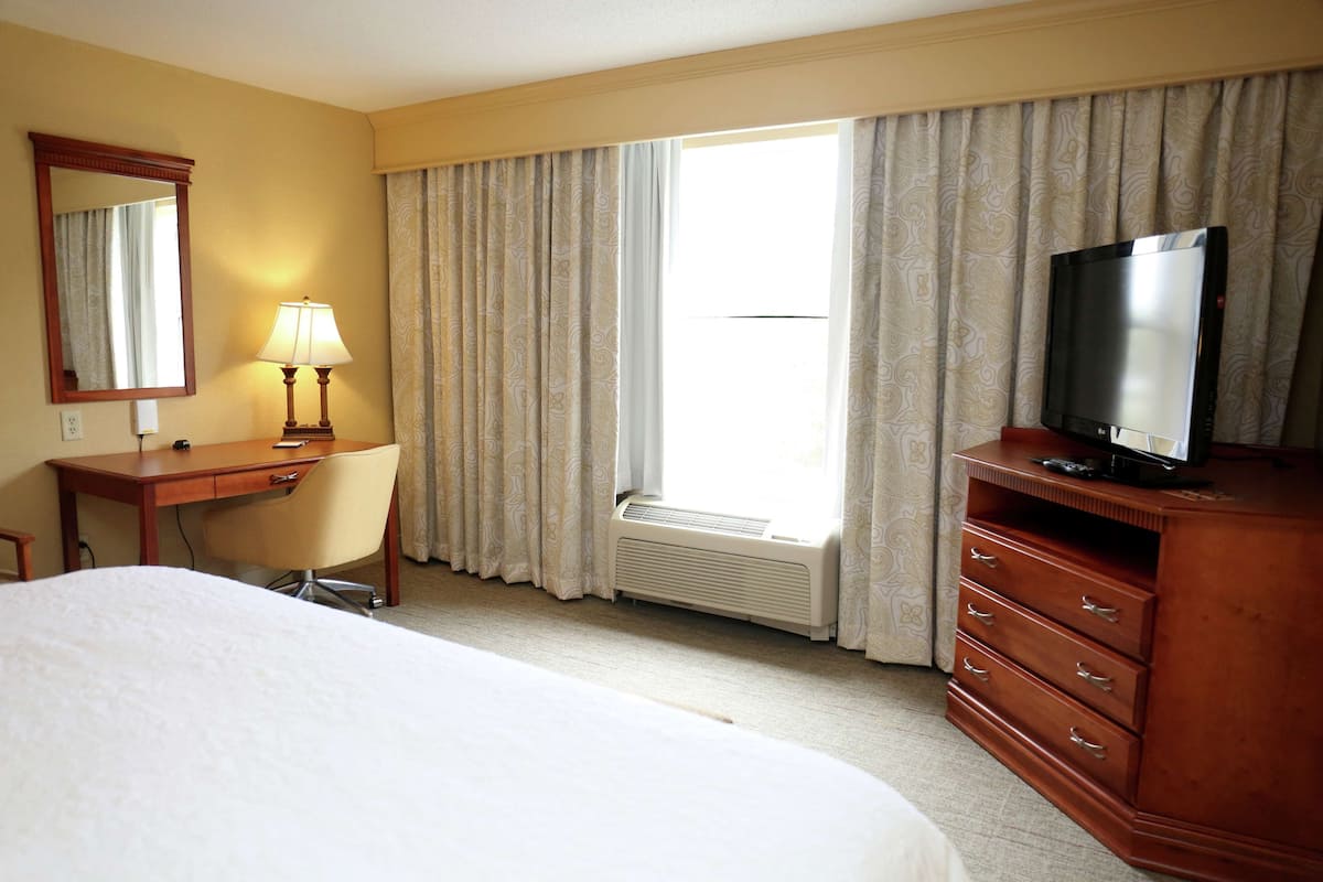 A hotel room with a bed, a desk, a chair, a television, and a window with curtains.