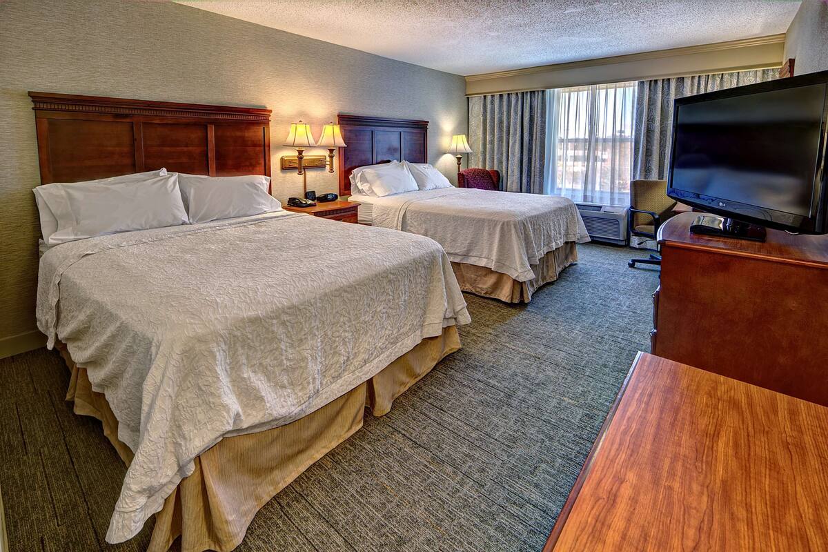 A hotel room with two beds, a television, and a desk.