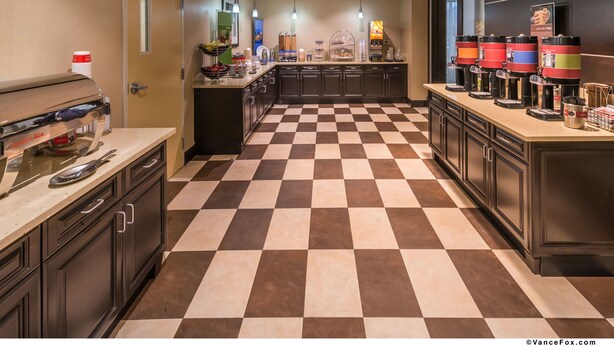 A hotel kitchen with a checkered floor, a coffee station, and a fruit bowl.