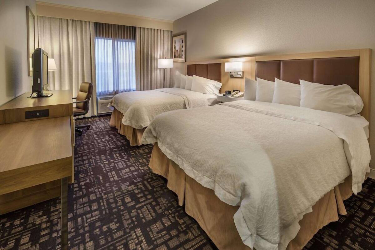 A hotel room with two beds, a desk, a chair, a television, and a window with curtains.
