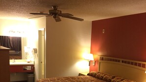 Una habitación de hotel con cama, escritorio, silla, lámpara y ventilador de techo.