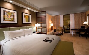 A hotel room with a large bed, a desk, a chair, and a sofa. There are two lamps on the desk and a window with curtains. - The Signature at MGM Grand (All Suites) (Las Vegas)