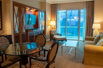 A hotel room with a large bed, a small table, a bench, a chair, a desk, a TV, and a view of the city at night. at The Signature at MGM Grand (All Suites)