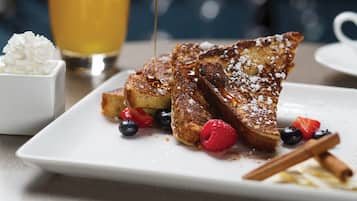 French toast with berries and powdered sugar, syrup, and a cinnamon stick on a plate.