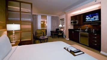 A hotel room with a bed, a desk, a chair, a television, and a kitchenette.