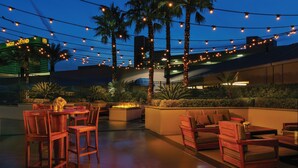 An outdoor patio area with wooden furniture, a fire pit, and string lights.