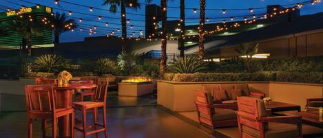 An outdoor patio area with wooden furniture, a fire pit, and string lights.