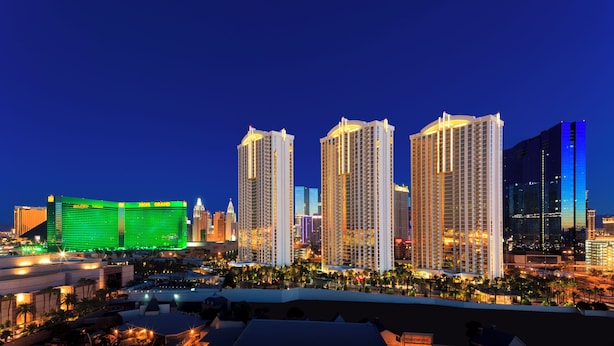 A city skyline at night with illuminated high-rise buildings, including a prominent hotel with a green facade.