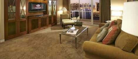 Habitación de hotel con televisor de pantalla plana grande, sofá, una mesita de café y vista a un paisaje urbano a través de la ventana.