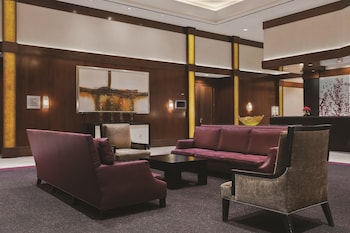 A kitchen with wooden cabinets, a stainless steel microwave, and a refrigerator. There are two bar stools and a framed painting on the wall. at The Signature at MGM Grand (All Suites)