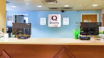 Zona de recepció d'hotel amb un cartell de 'Quality by Choice Hotels', dos monitors, una planta i un cartell que diu 'Només personal'.
