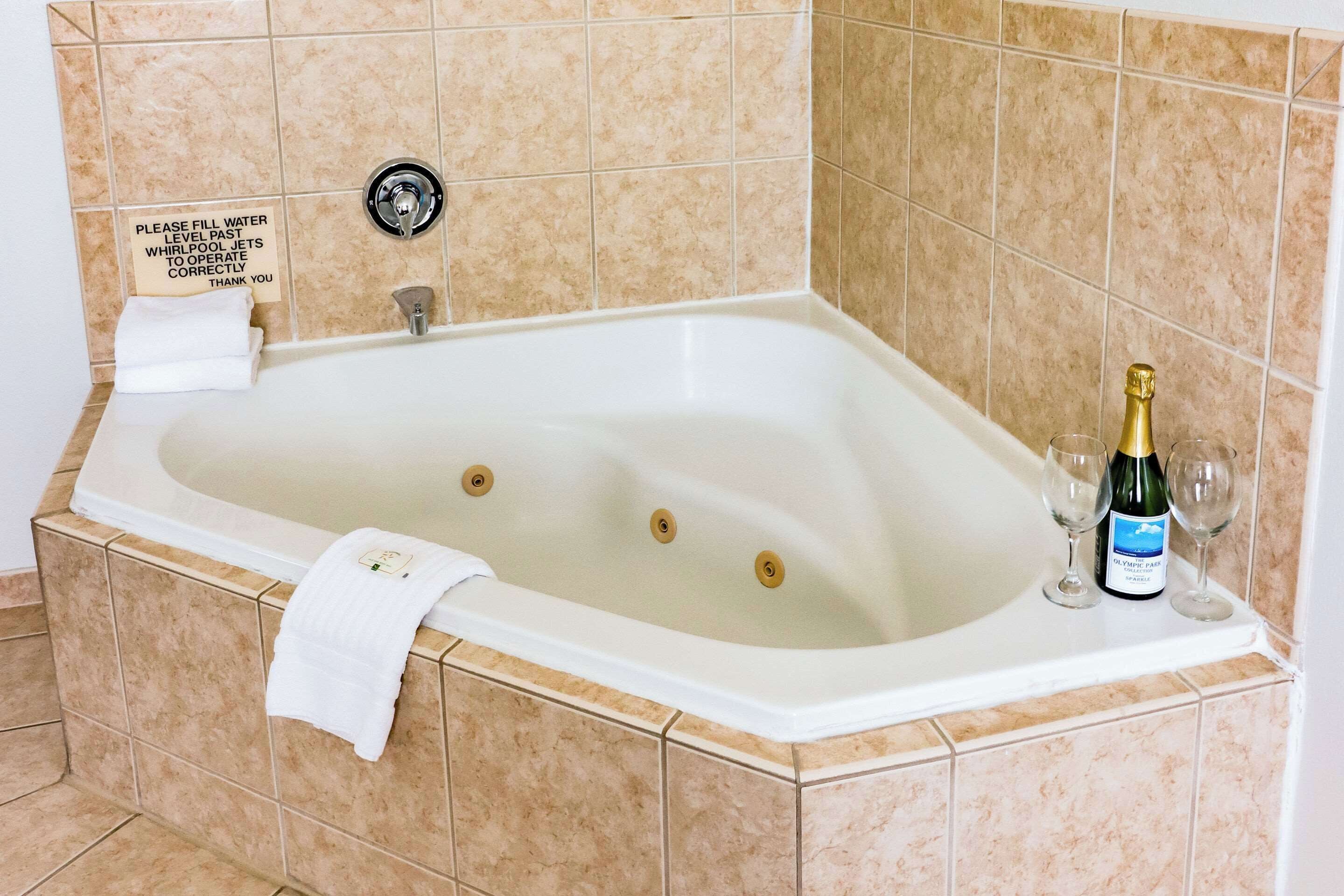 Una bañera con un letrero que indica llenar el agua más allá de los jets de hidromasaje para un correcto funcionamiento, una botella de champán y dos copas al borde.