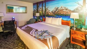 A hotel room with a large bed, a desk with a chair, a nightstand, and a wall mural of a mountain landscape. - Quality Inn & Suites Sequim at Olympic National Park (Sequim)