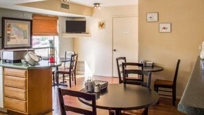 A dining area with a round table and chairs, a kitchen counter with a microwave, and a television on the wall. - Rodeway Inn Silver Creek Inn (Snowflake)