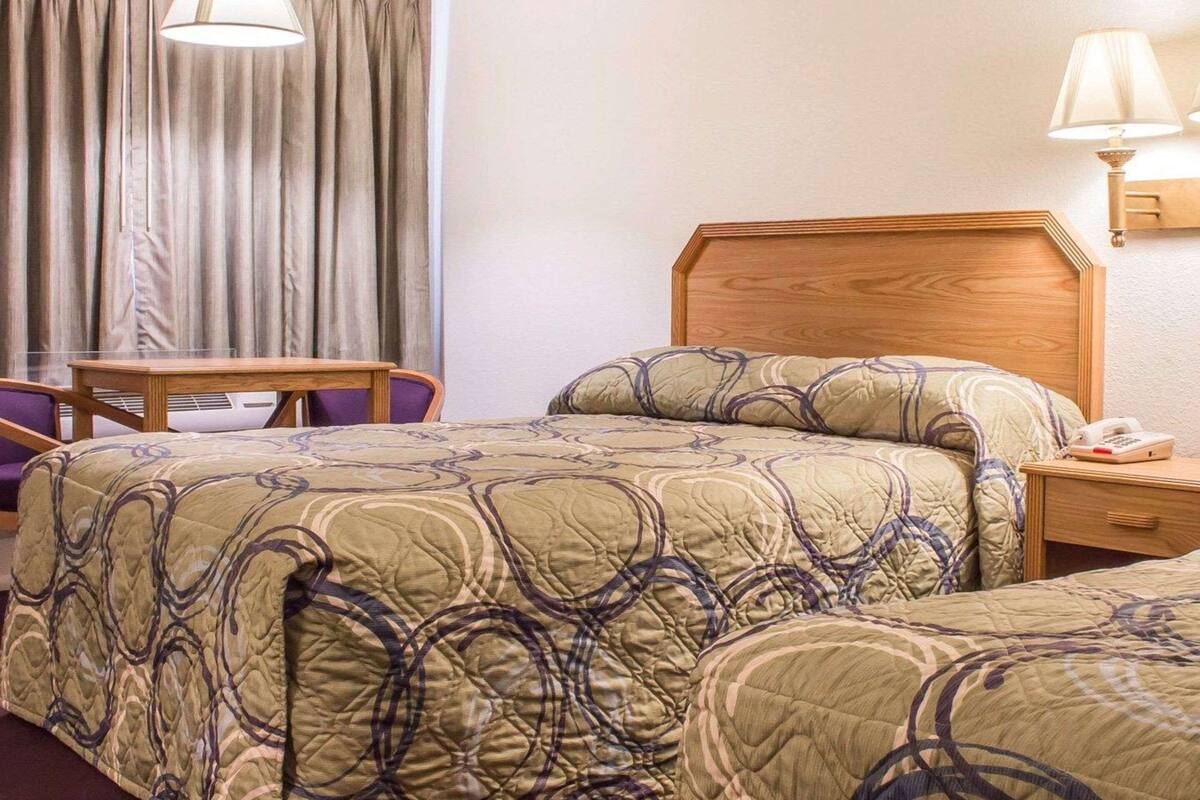 A hotel room with two beds, a wooden headboard, a desk, a chair, and a telephone.