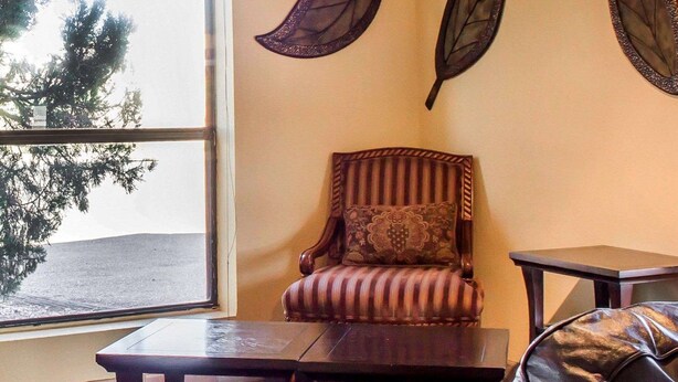 A room with a view of a beach, a leather sofa, a striped armchair, and a small table. - Rodeway Inn Silver Creek Inn (Snowflake)