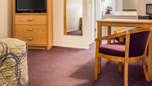 A room with a wooden TV stand, a mirror, a dining table with chairs, and a bed with a patterned blanket. - Rodeway Inn Silver Creek Inn (Snowflake)