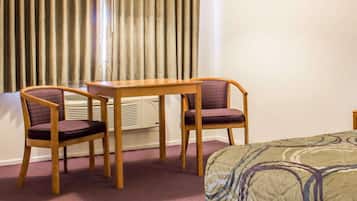 Una habitación de hotel con una cama, dos sillas, una mesita y un ventanal con cortinas.