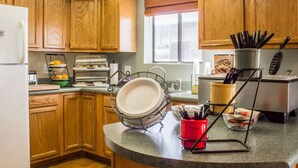 A kitchen with wooden cabinets, a built-in oven, a sink, and a window with blinds. - Rodeway Inn Silver Creek Inn (Snowflake)