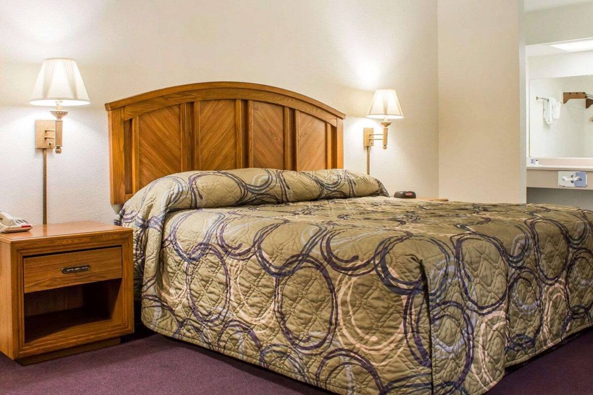 A hotel room with a wooden headboard, two bedside lamps, a bedside table with a lamp, a telephone, and a mirror on the wall.