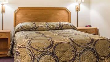 Habitación de hotel estándar con cabecera de madera, cama con colcha estampada, dos lámparas de noche y mesita con un reloj.