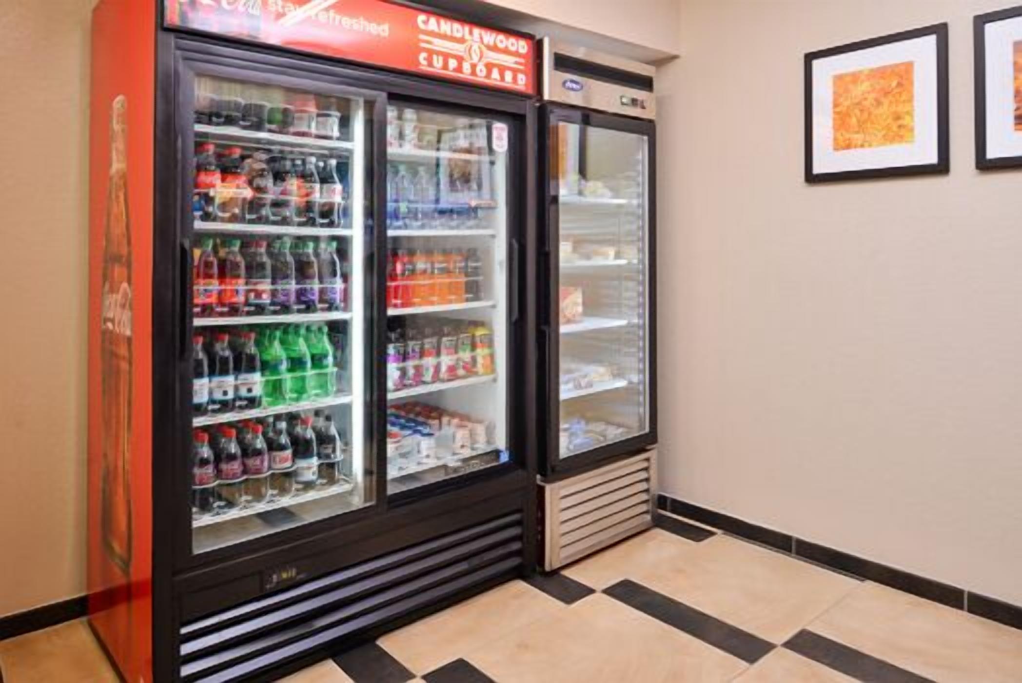 Máquina expendedora con diversas bebidas y aperitivos, ubicada en un pasillo con suelo de baldosas y cuadros en la pared.