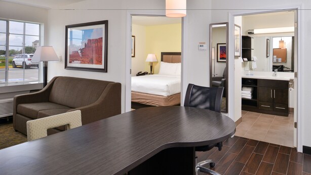 A hotel room with a large bed, a desk with a chair, a sofa, a bathroom with a mirror, and a window with a view of the outside. - Candlewood Suites Beaumont by IHG (Beaumont)