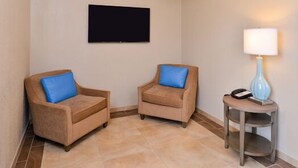 A room with two beige armchairs with blue cushions, a flat-screen TV on the wall, and a small table with a lamp and a phone. - Candlewood Suites Beaumont by IHG (Beaumont)