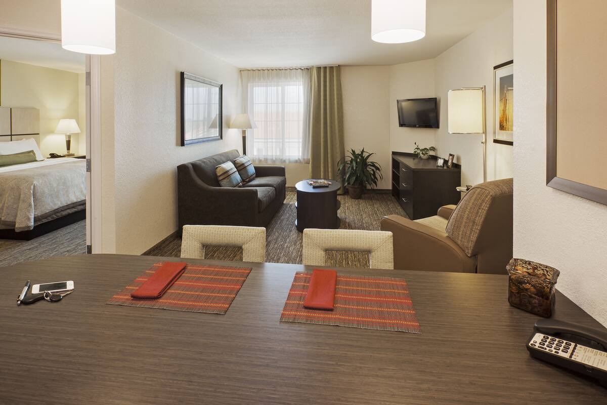 Ein Hotelzimmer mit Bett, Sofa, Schreibtisch mit zwei Stühlen, Fernseher, Pflanze und Schrank.