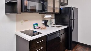 A modern kitchen with dark cabinetry, a black refrigerator, a microwave, and a built-in dishwasher. - Candlewood Suites Beaumont by IHG (Beaumont)