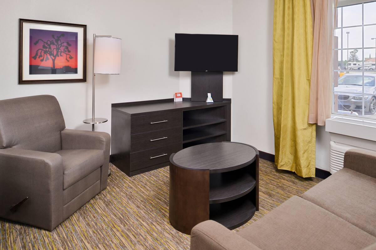 Ein Hotelzimmer mit einer Couch, einem Fernseher auf einem Schrank, einem kleinen Tisch und einem gemusterten Teppich.