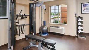 Un gimnasio con equipo de ejercicio, una banca y un ventanal con vistas al exterior.