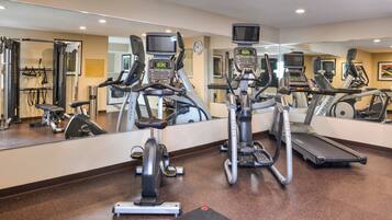 A gym with multiple exercise machines, a large mirror, and a clock on the wall.