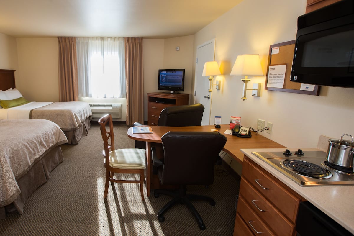 Ein Hotelzimmer mit zwei Betten, einem Schreibtisch mit Stuhl, einem Fernseher, einer Mikrowelle und einer kleinen Küchenzeile.