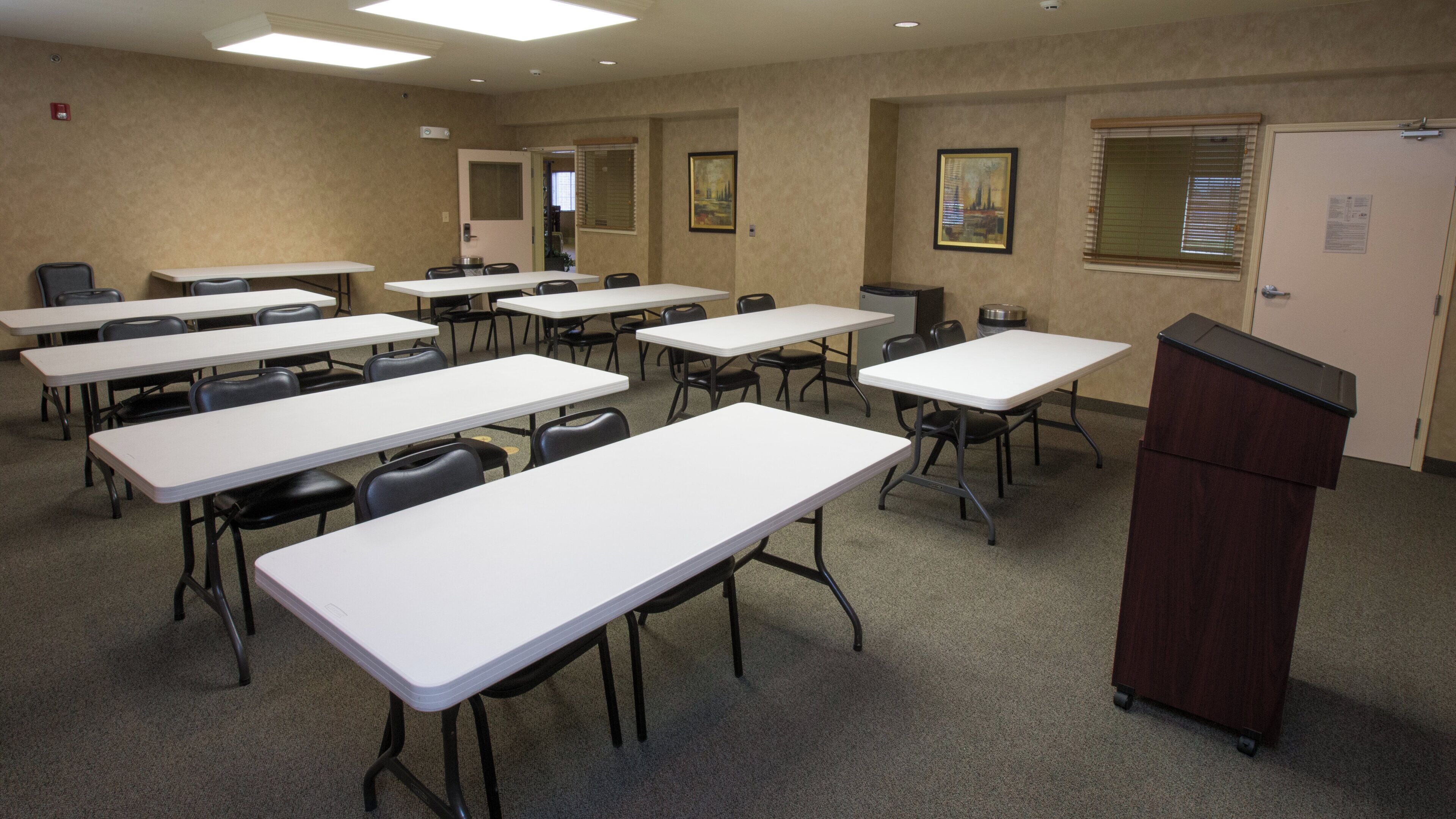 Une salle de conférence équipée de plusieurs tables et chaises, d’un pupitre et de tableaux encadrés aux murs.