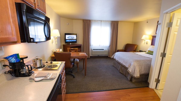 Hotelkamer met kitchenette, een bed, bureau, televisie en raam met gordijnen.