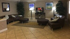 Un salon avec un canapé en cuir marron, un pouf rond, une table basse, un téléviseur posé sur un meuble et deux lampadaires.
