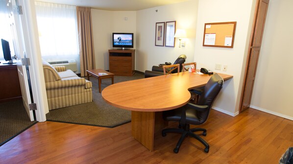 Une chambre d’hôtel avec une table à manger en bois, un canapé, une télévision et un bureau avec une lampe.