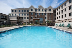 A swimming pool with a gazebo in the center, surrounded by a fence and lounge chairs.