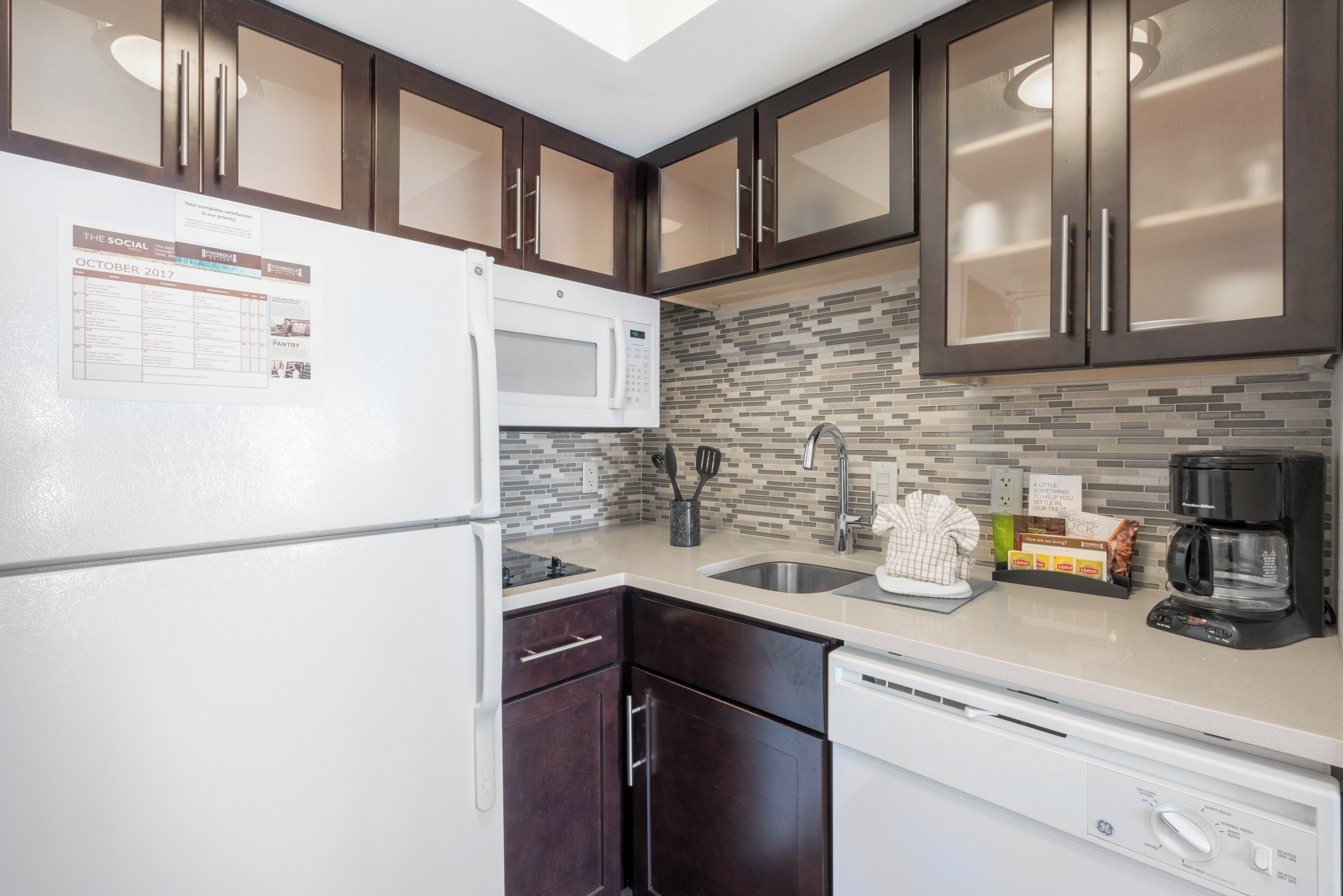 A kitchen with dark wooden cabinets, a white refrigerator, a microwave, a sink, and a dishwasher.