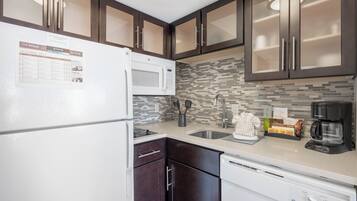 A kitchen with dark wooden cabinets, a white refrigerator, a microwave, a sink, and a dishwasher.