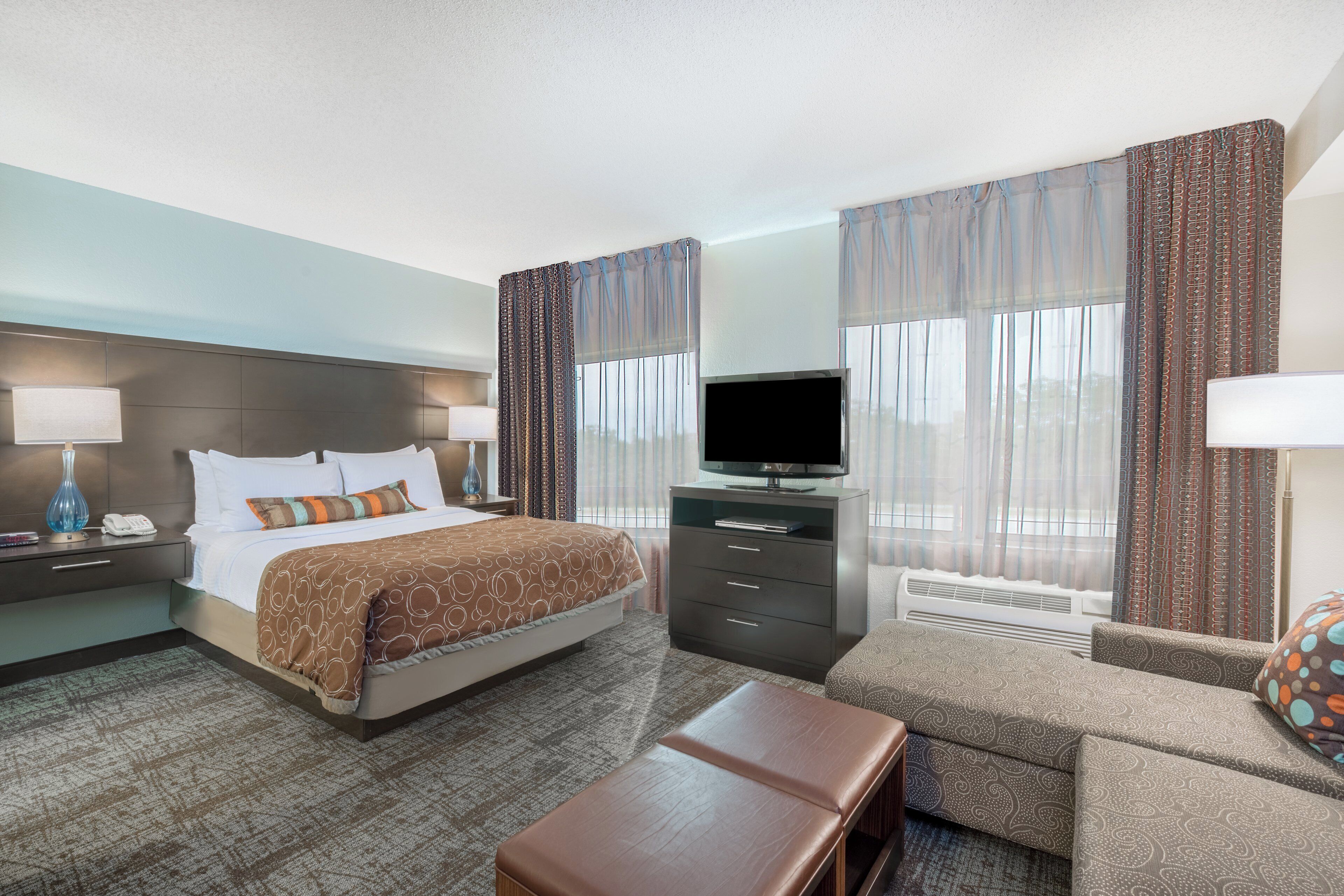 A hotel room with a bed, a TV, a desk, a chair, and a sofa.