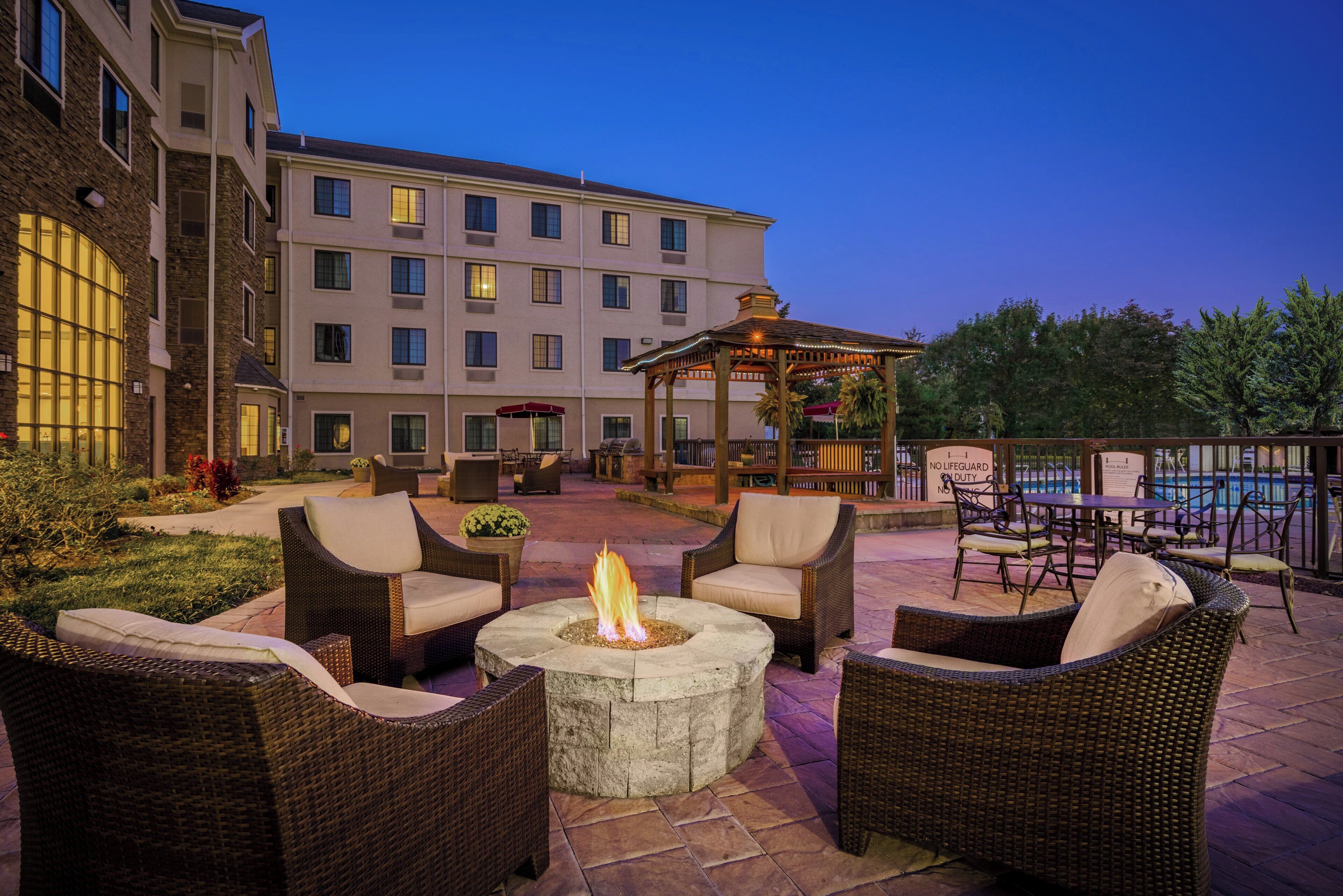 A patio area with wicker furniture, a fire pit, and a pool in the background.