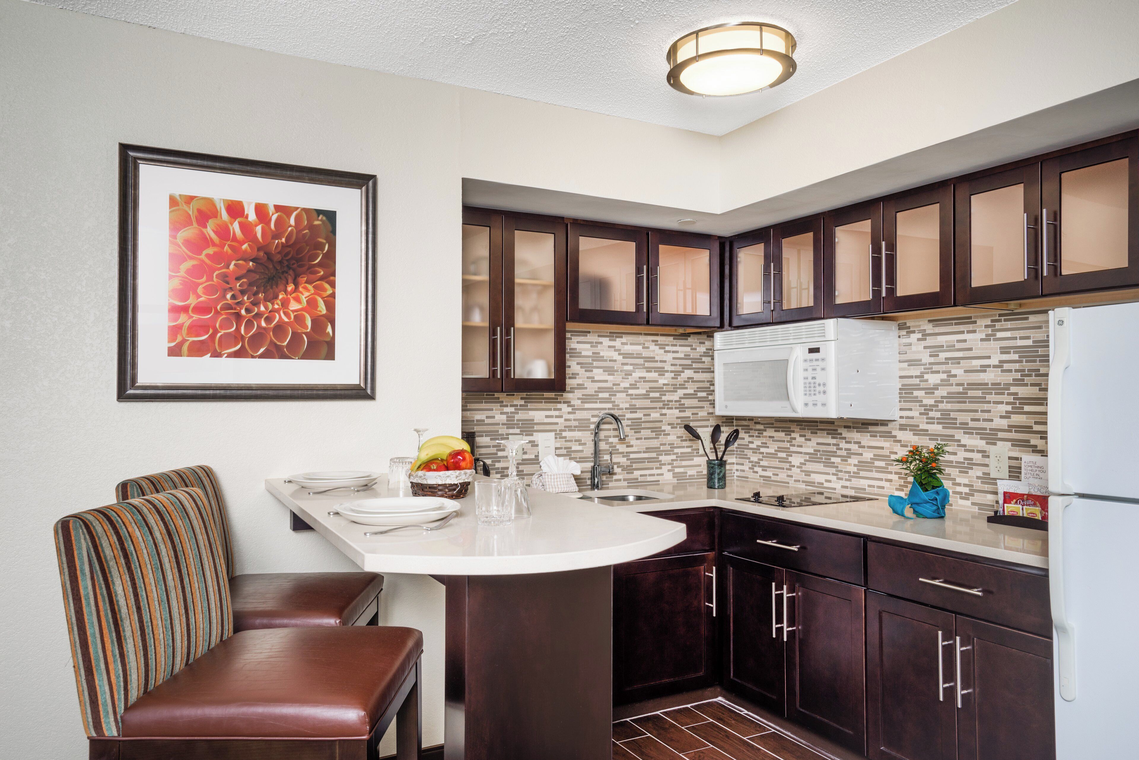 A kitchen with dark wood cabinets, a white microwave, and a tiled backsplash.